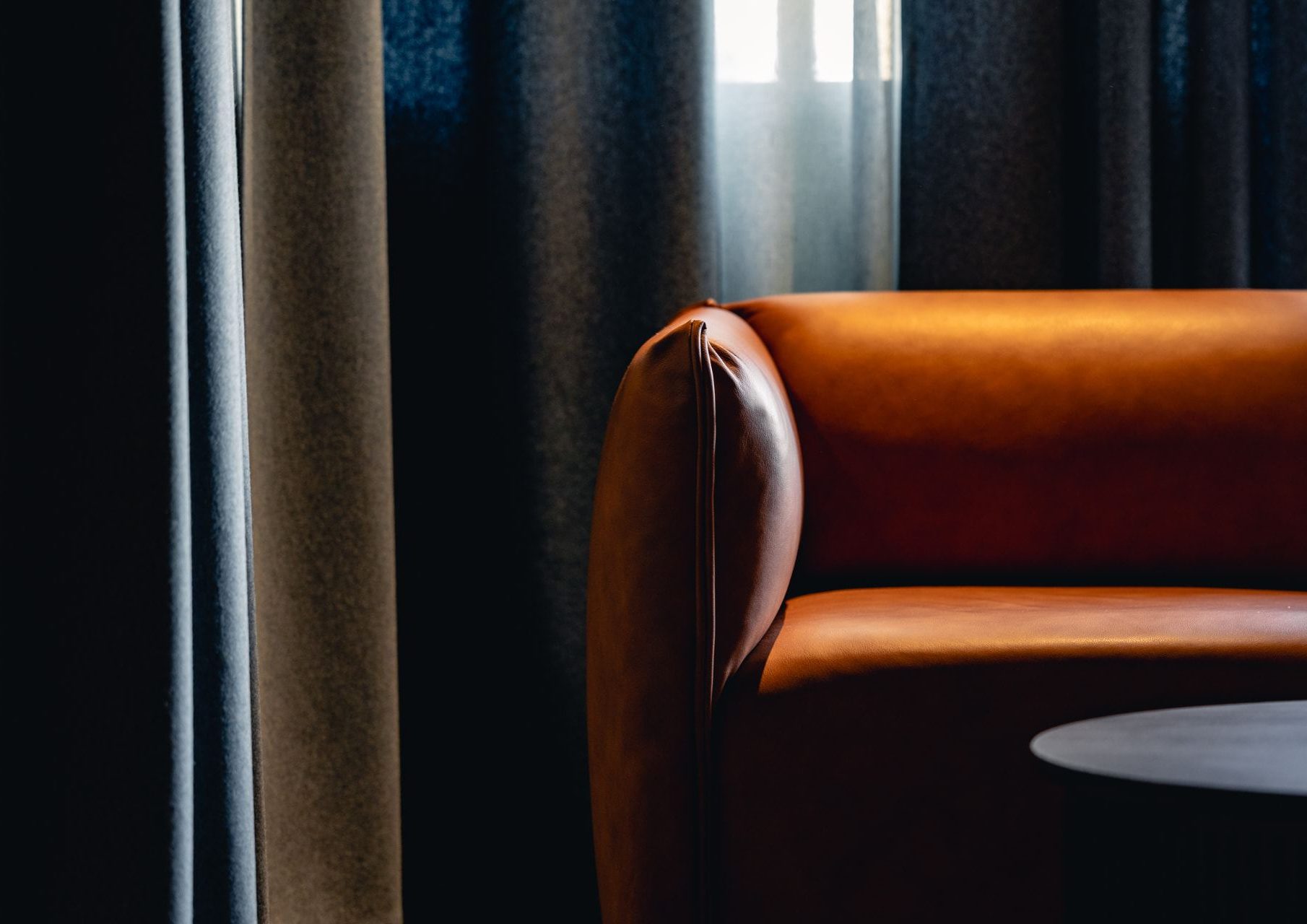 Mörk hotellounge med möbler i cognacläder och mjukt ljus genom gardiner